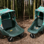 Two zoo Atlanta branded strollers sitting on mulch in front of a sand of bamboo.