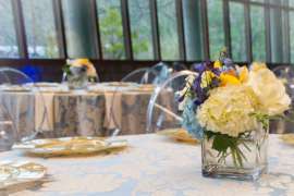 Flower arrangements on a well-decorated tables in a room with a wall of windows.