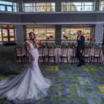 A couple dressed in formal attire pose in front of a set table in the Carlos Ballroom.