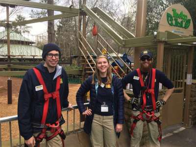 A group of three Zoo Atlanta teammates pose in front of the aerial ropes course.