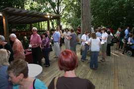A large group of guest stand about on the deck by the gorilla habitat, some of them waiting in line at a food table.
