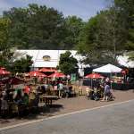 People lounge about a an area of the zoo in front of a large tent featuring tables and umbrellas and a smaller tent with food to purchase.