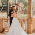 a bridge and groom kiss in front of the giraffe habitat