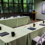 Tables set-up in a u-shape with folders and coffee mugs in a meeting room.
