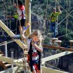 Three children navigate an outdoor ropes course.