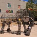 A life size statue of an elephant made of open wire stands in front a building decorated in African inspired patterns.